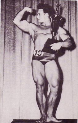 Steve Reeves hits a biceps shot while holding trophy.